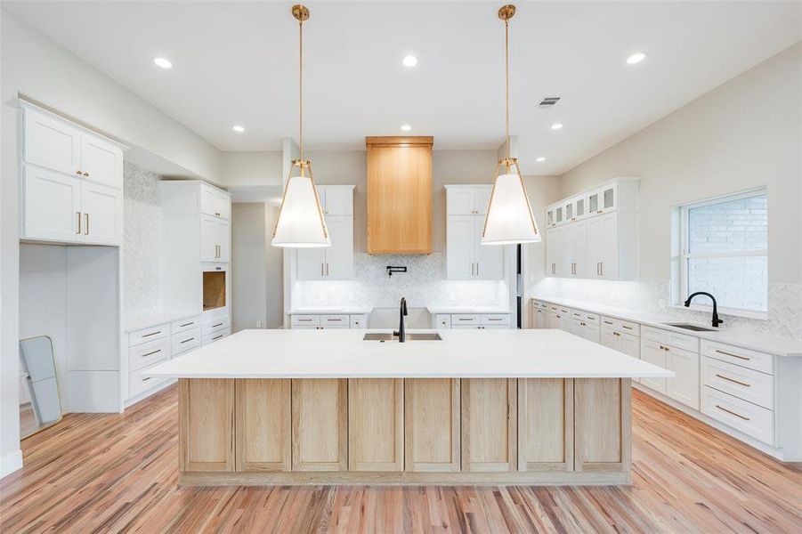 Kitchen featuring light wood-type flooring, a spacious island, light stone countertops, backsplash, and recessed lighting