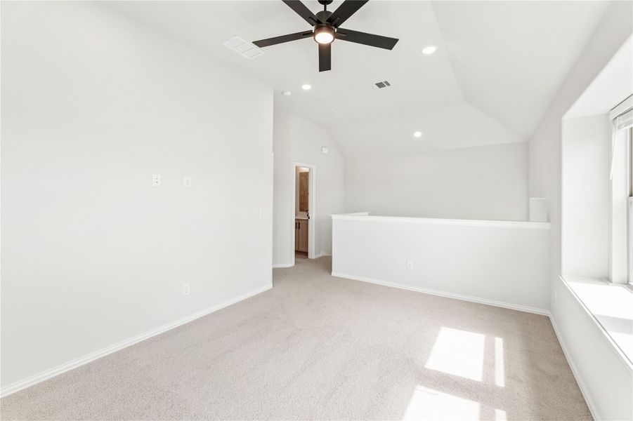 Empty bedroom with vaulted ceiling, ceiling fan, carpet flooring, and ensuite bathroom doorway visible