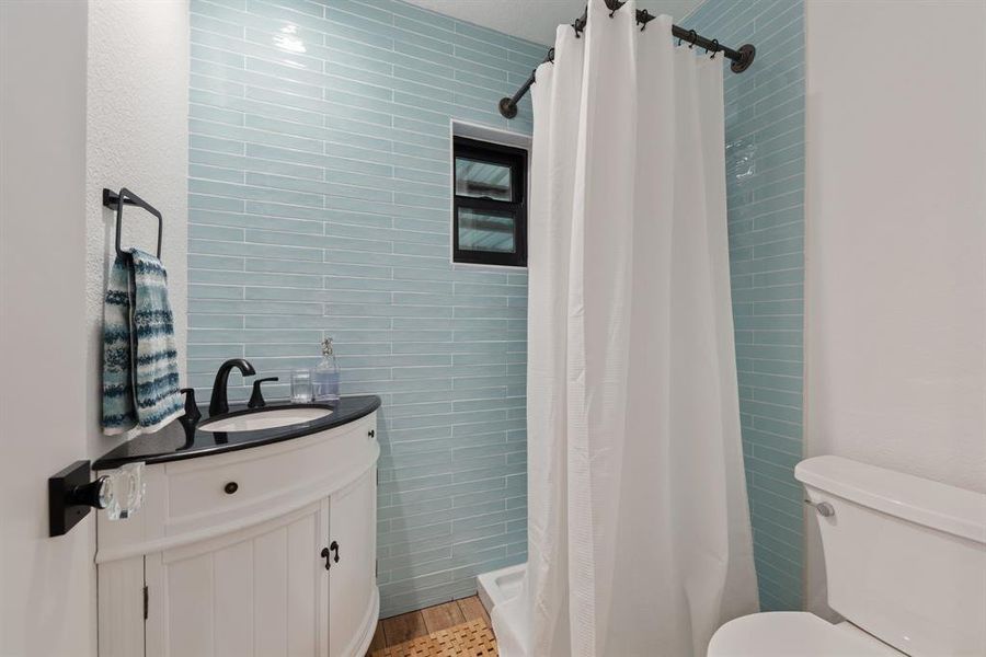 Full bath by the living and kitchen area with all-new corner-set vanity, fixture, and beautifully tiled shower area.