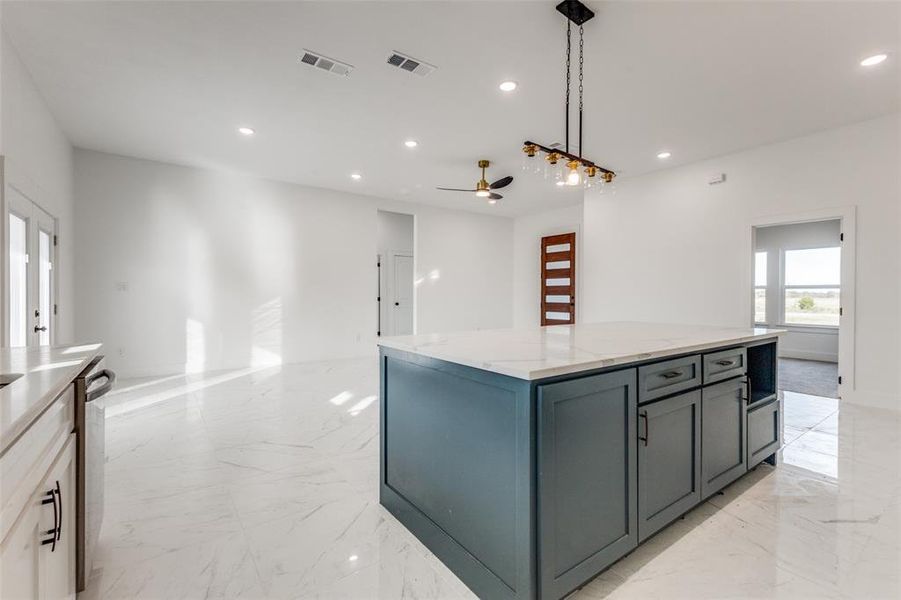 Kitchen featuring light stone countertops, ceiling fan, gray cabinets, a kitchen island, and hanging light fixtures