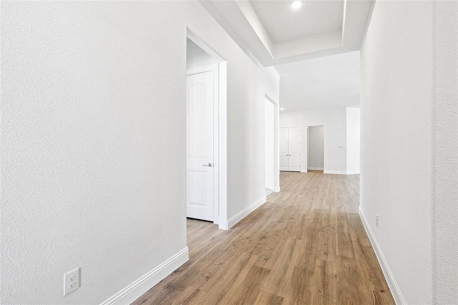 Hall featuring light wood-type flooring, a raised ceiling, and recessed lighting