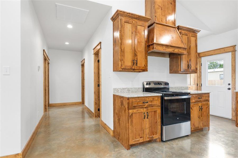 Kitchen with stainless steel electric range oven, finished concrete flooring, baseboards, brown cabinetry, and recessed lighting Kitchen with stainless steel electric range oven, finished concrete flooring, baseboards, brown cabinetry, and recessed lighting