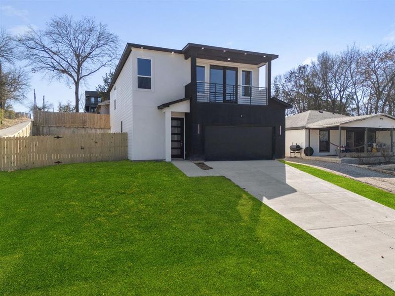 View of front of property featuring a garage, a front lawn, and a balcony