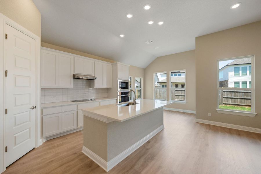 Kitchen with recessed lighting, a kitchen island with sink, tasteful backsplash, lofted ceiling, and white cabinetry