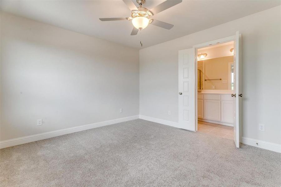 Unfurnished bedroom featuring light colored carpet, ceiling fan, and ensuite bathroom