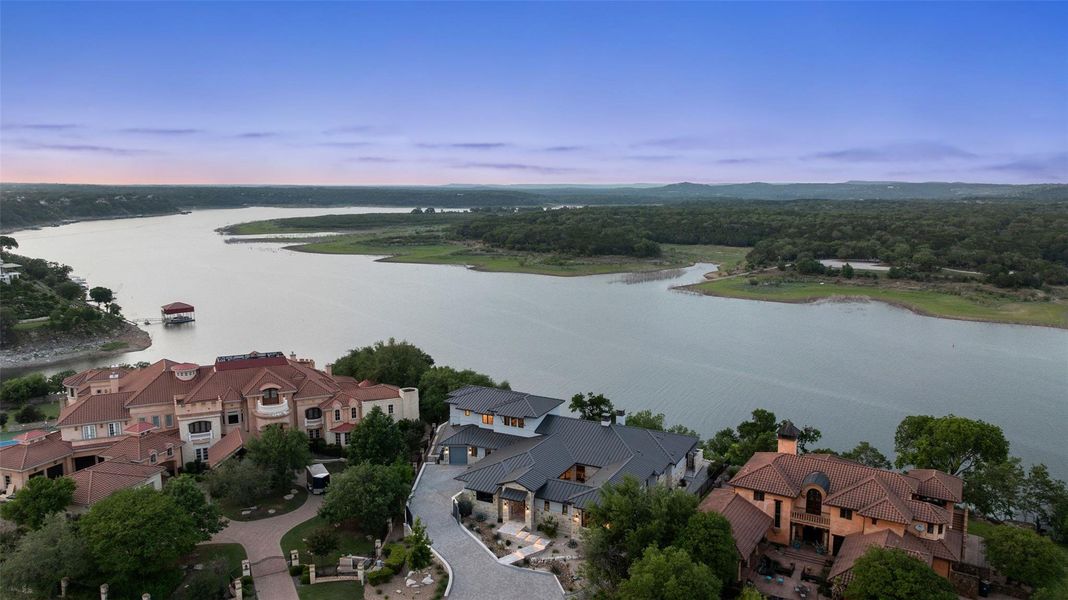 Panoramic aerial displaying multiple properties with a natural body of water and wooded areas