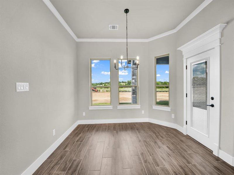 Unfurnished dining area with wood finish floors, a chandelier, and crown molding Unfurnished dining area with wood finish floors, a chandelier, and crown molding