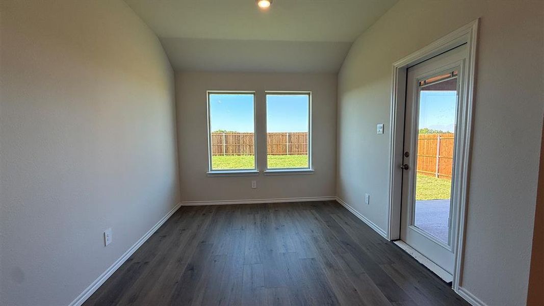 Spacious room featuring wood-finish flooring, neutral wall tones, and vaulted ceilings