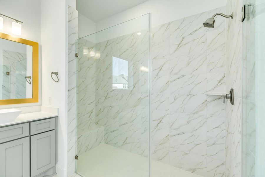This oversized walk-in glass shower features elegant tile flooring and wall finishes.