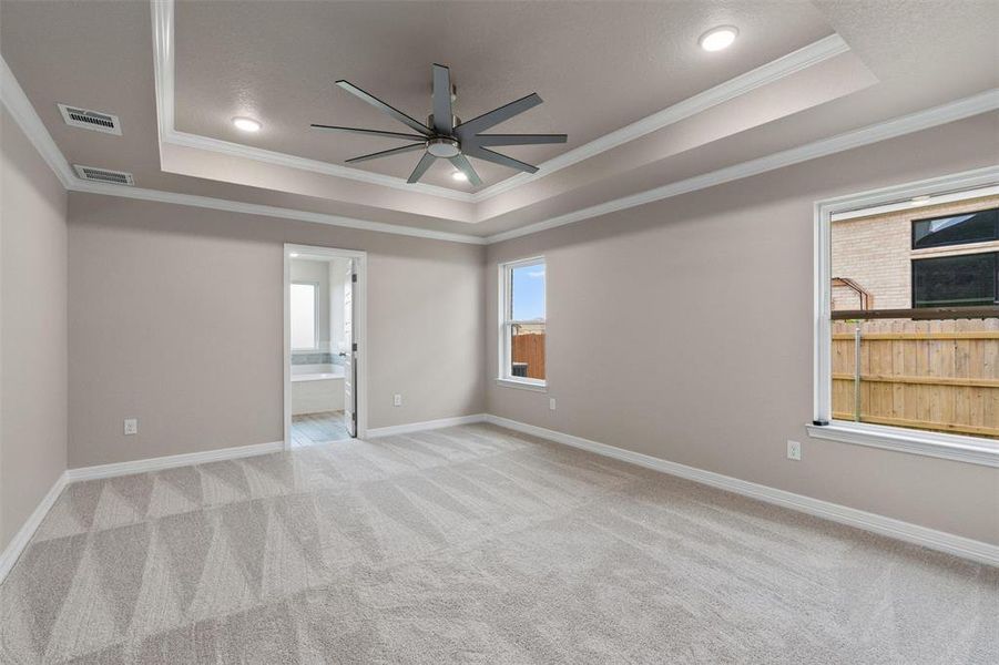 Spacious bedroom featuring light-toned carpeting and a tray ceiling with recessed lighting Spacious bedroom featuring light-toned carpeting and a tray ceiling with recessed lighting