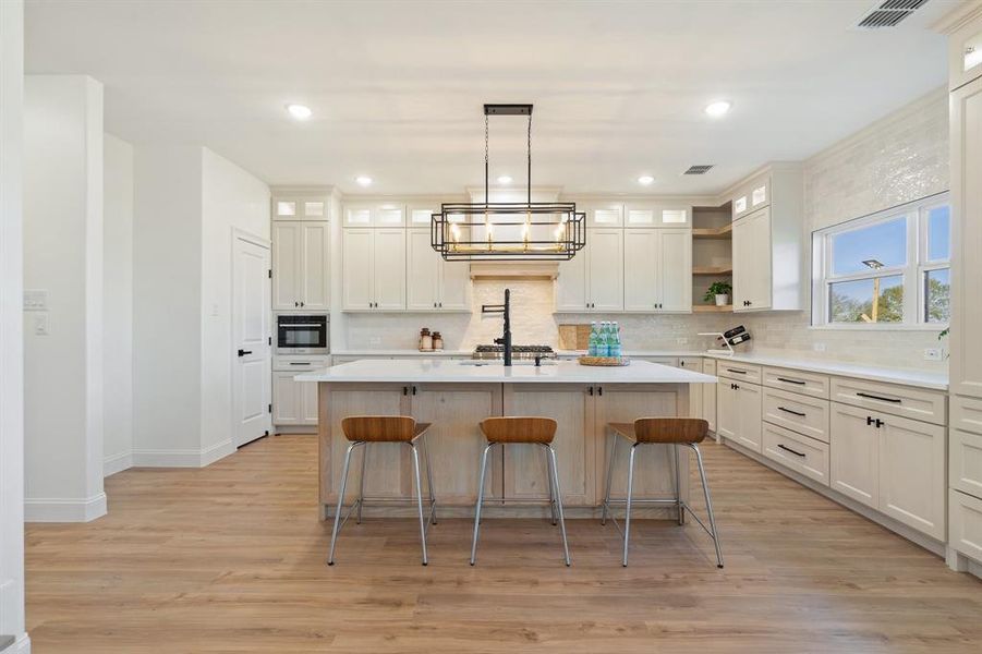 Kitchen featuring glass insert cabinets, a kitchen breakfast bar, pendant lighting, light wood-type flooring, and recessed lighting Kitchen featuring glass insert cabinets, a kitchen breakfast bar, pendant lighting, light wood-type flooring, and recessed lighting