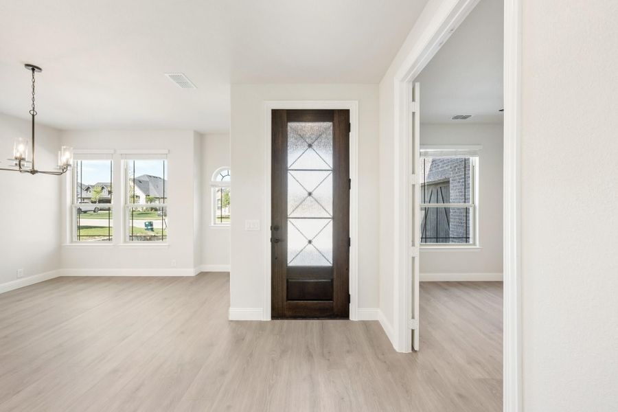 Open entryway with dark wood glass-panel front door, light hardwood floors, and chandelier nearby.