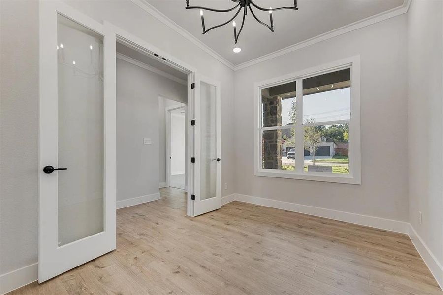 Empty room with ornamental molding, light wood-type flooring, suspended lighting, and french doors
