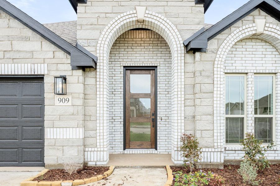 Home entrance with arched brick surround, wood and glass front door, and dark garage door