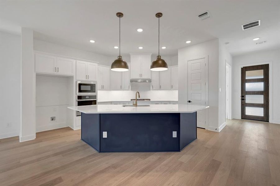 Two tone kitchen featuring a kitchen island with sink, stainless steel oven, light wood-style floors, built in microwave, and two tone cabinets