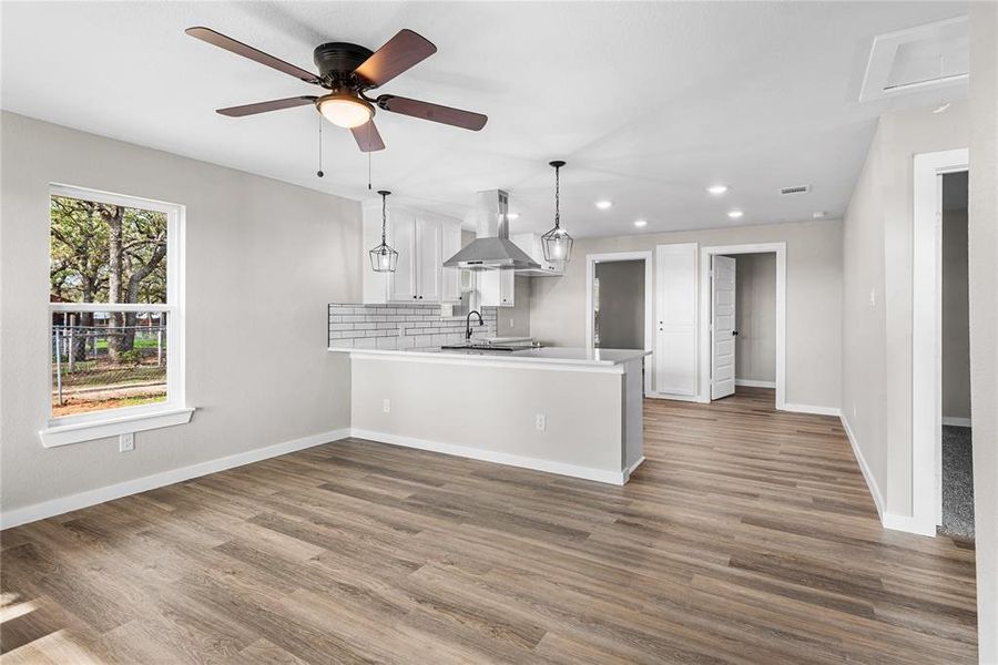 Kitchen featuring a peninsula, recessed lighting, island exhaust hood, backsplash, and dark wood-style flooring