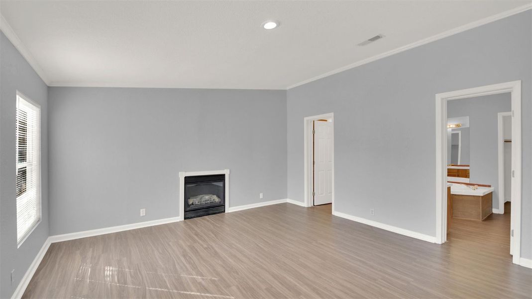 Unfurnished living room with a glass covered fireplace, crown molding, light wood-type flooring, and recessed lighting