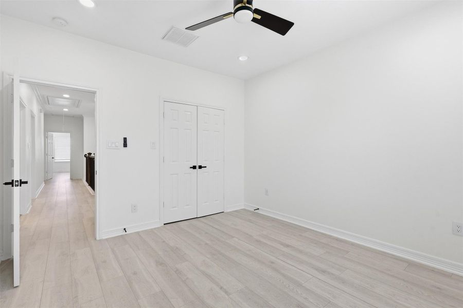 Spacious second floor bedroom with ceiling fan, white walls, and light wood look flooring.