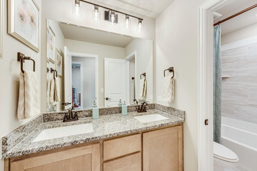 Bathroom with double sink vanity, granite countertops, wood cabinets, and tiled shower with curtain