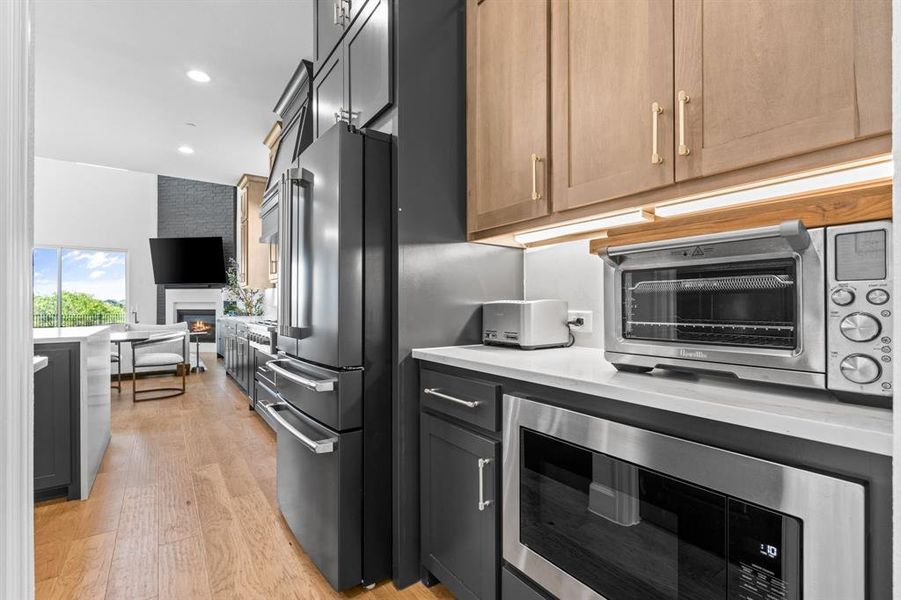 Kitchen featuring stainless steel microwave, a fireplace, high end fridge, recessed lighting, and light wood-style flooring Kitchen featuring stainless steel microwave, a fireplace, high end fridge, recessed lighting, and light wood-style flooring