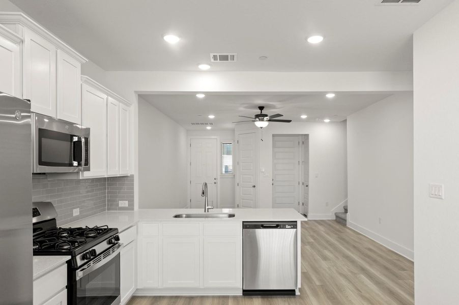 Kitchen featuring appliances with stainless steel finishes, white cabinets, a peninsula, backsplash, and ceiling fan