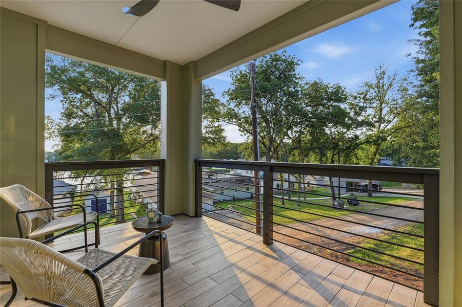 Covered balcony with wood-finish flooring, featuring a modern ceiling fan and cable railings Covered balcony with wood-finish flooring, featuring a modern ceiling fan and cable railings