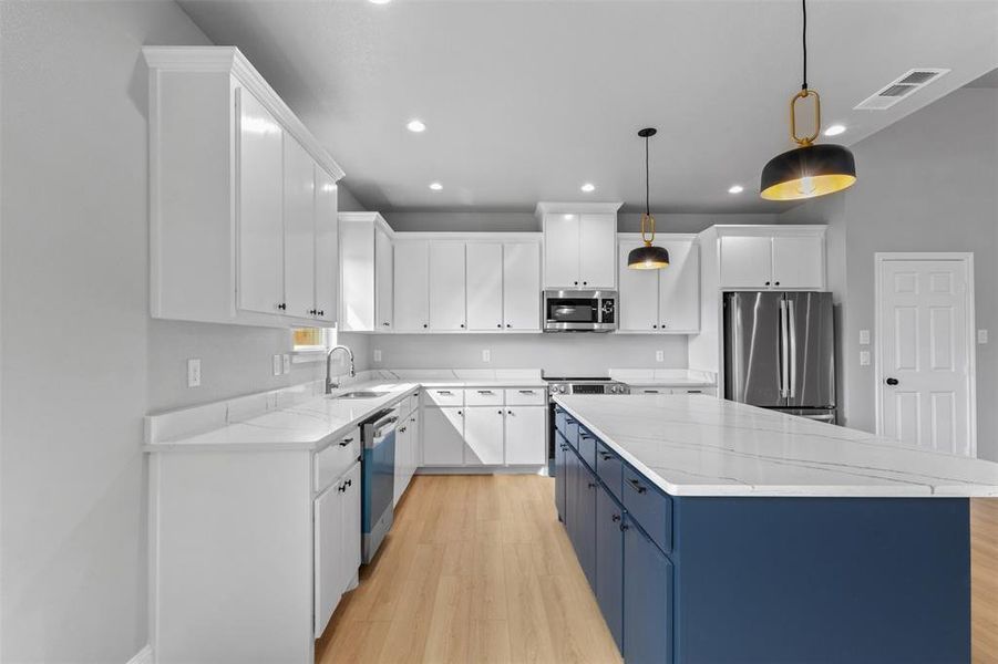 Kitchen featuring blue cabinets, white cabinets, light stone countertops, appliances with stainless steel finishes, and recessed lighting