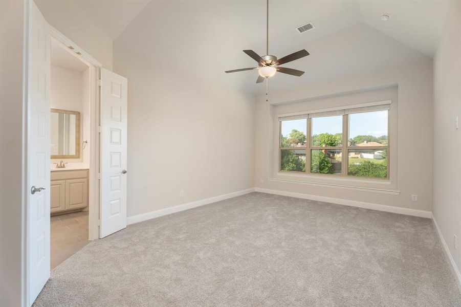 Unfurnished bedroom featuring light carpet, lofted ceiling, a ceiling fan, and ensuite bath