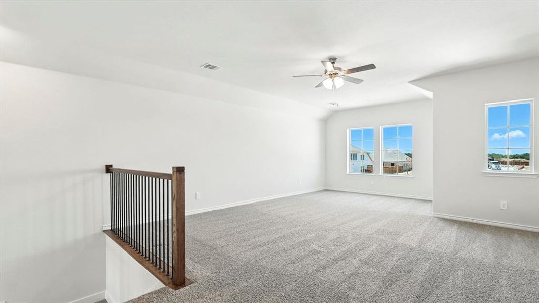 Spacious carpeted room featuring a ceiling fan, three windows, and a wood and metal railing overlooking a lower level