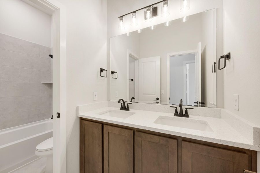 Bathroom with double sink vanity, wood cabinets, quartz countertop, and tiled tub-shower combo