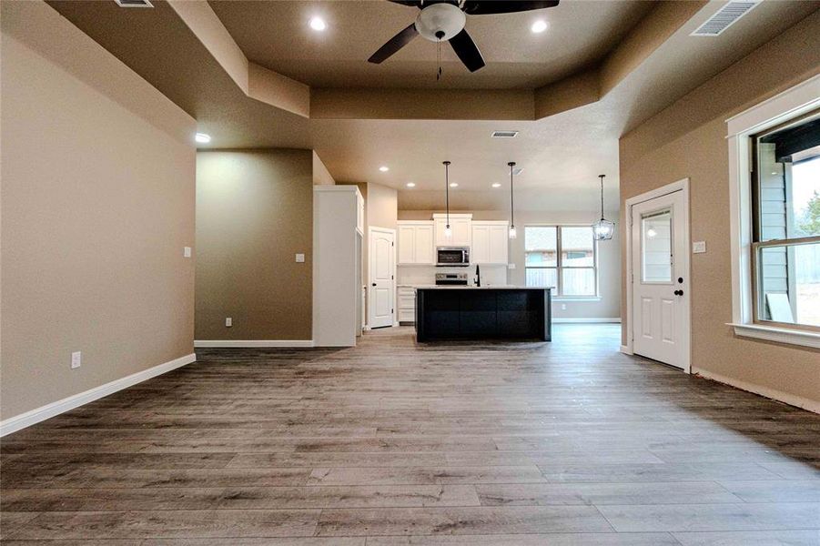 Kitchen featuring decorative light fixtures, white cabinets, a kitchen island with sink, light hardwood / wood-style floors, and a tray ceiling