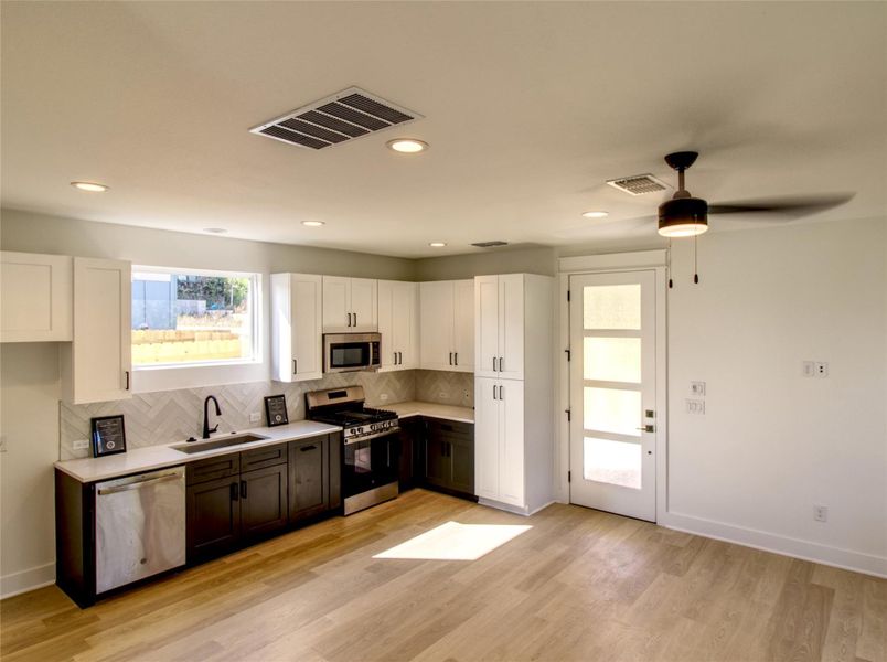 Kitchen featuring white cabinetry, stainless steel appliances, decorative backsplash, light wood-type flooring, and a ceiling fan Kitchen featuring white cabinetry, stainless steel appliances, decorative backsplash, light wood-type flooring, and a ceiling fan