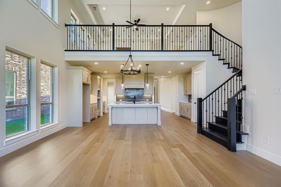 Kitchen with pendant lighting, a kitchen island with sink, light countertops, light wood-style floors, and a towering ceiling