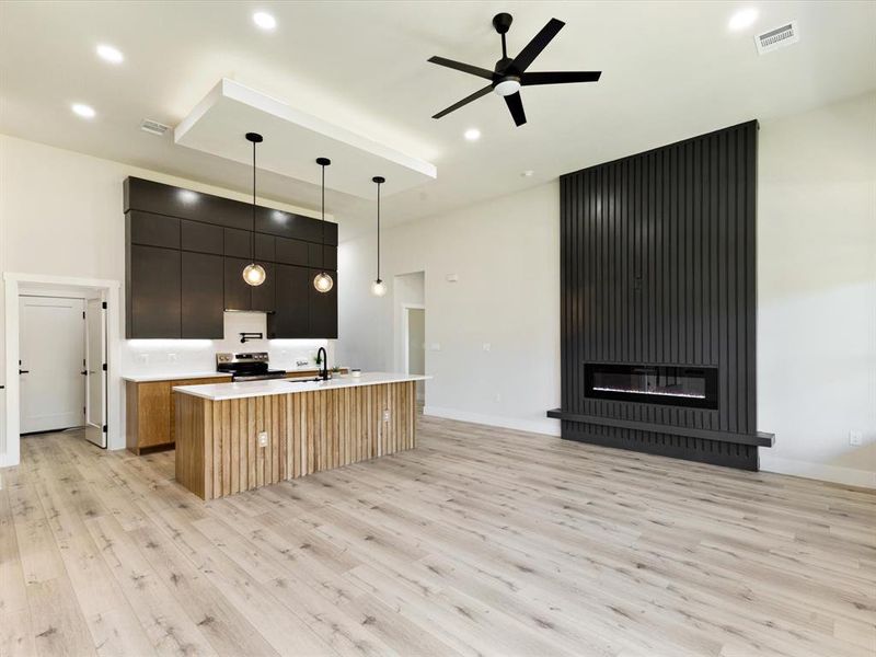 Kitchen with modern cabinets, a center island with sink, a fireplace, pendant lighting, and open floor plan