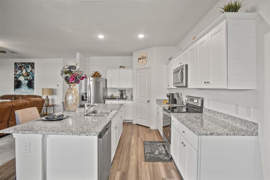 Kitchen with appliances with stainless steel finishes, open floor plan, light wood finished floors, white cabinets, and a center island with sink