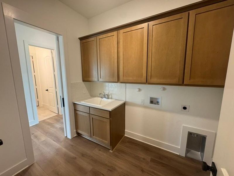 Utility room featuring wood-finish flooring, custom wood cabinetry, a built-in utility sink with white countertop, and a white tile backsplash
