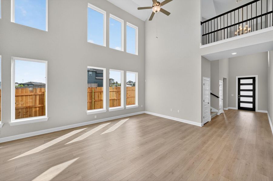Unfurnished living room featuring a high ceiling, light wood-style flooring, and ceiling fan Unfurnished living room featuring a high ceiling, light wood-style flooring, and ceiling fan