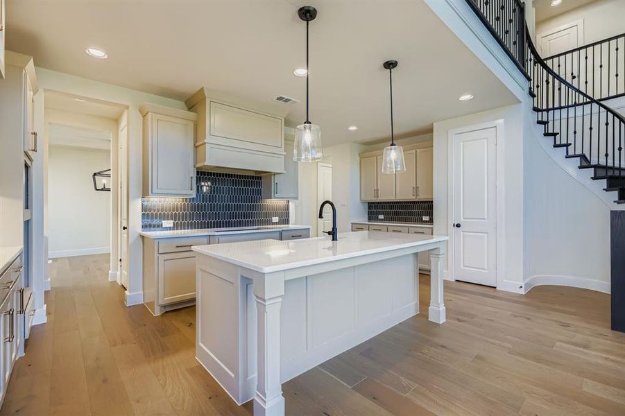 Kitchen with decorative light fixtures, recessed lighting, decorative backsplash, light wood finished floors, and a kitchen island with sink