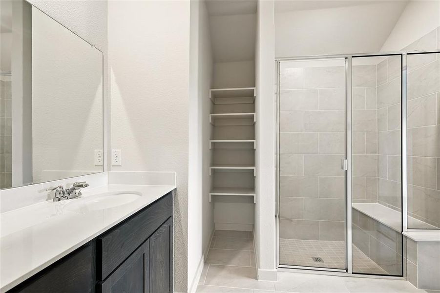 Bathroom featuring a stall shower, vanity, light tile patterned flooring, and a walk in closet Bathroom featuring a stall shower, vanity, light tile patterned flooring, and a walk in closet