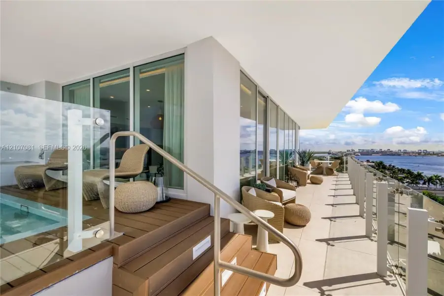 Expansive terrace featuring a raised wood-finish deck, a built-in plunge pool, floor-to-ceiling glass wall panels, a glass railing system, and metal handrails Expansive terrace featuring a raised wood-finish deck, a built-in plunge pool, floor-to-ceiling glass wall panels, a glass railing system, and metal handrails