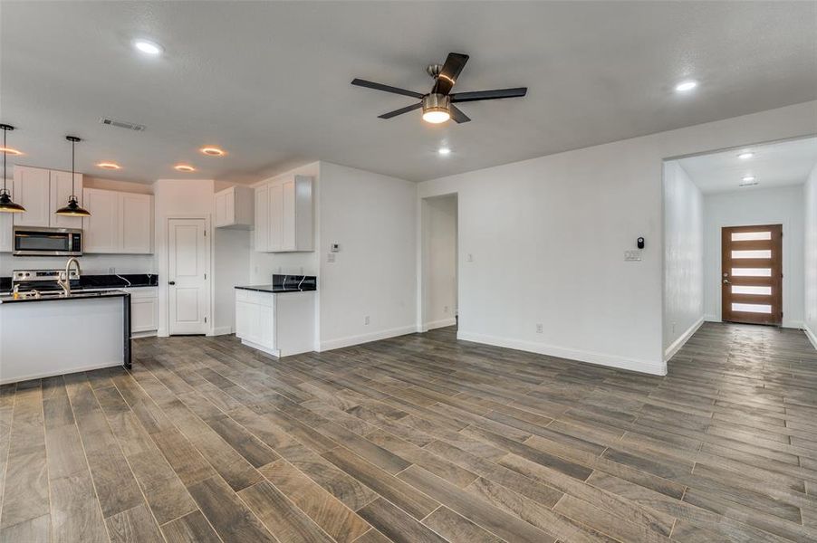 Kitchen with open floor plan, hanging light fixtures, dark wood-style floors, appliances with stainless steel finishes, and white cabinets Kitchen with open floor plan, hanging light fixtures, dark wood-style floors, appliances with stainless steel finishes, and white cabinets