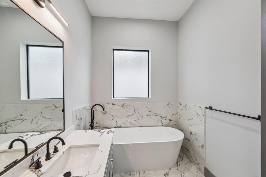 Deep soaking tub that serves as the centerpiece of this bathroom. Dual sinks with dark fixtures balance style and utility, while frosted windows bring in soft, natural light with privacy. Deep soaking tub that serves as the centerpiece of this bathroom. Dual sinks with dark fixtures balance style and utility, while frosted windows bring in soft, natural light with privacy.
