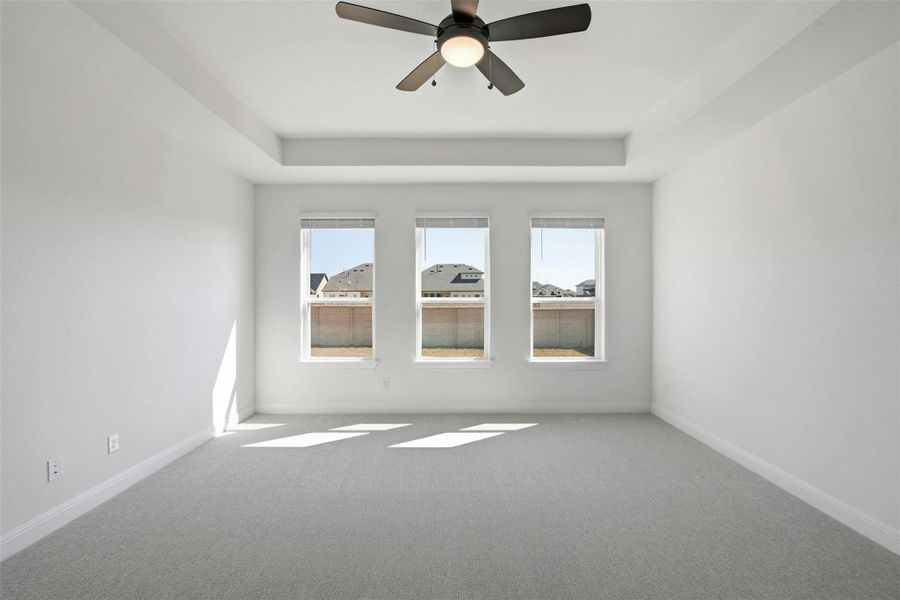 Carpeted empty room featuring ceiling fan and a tray ceiling