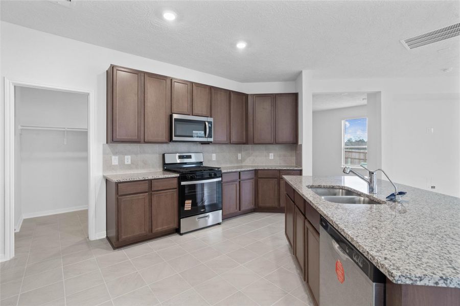 A true chef’s dream, this spacious and open kitchen boasts high ceilings, recessed lighting, rich stained wood cabinets, granite countertops, stainless steel appliances, a modern tile backsplash, extended counter space, an island, and a walk-in pantry—all with a clear view of the spacious Great Room.
