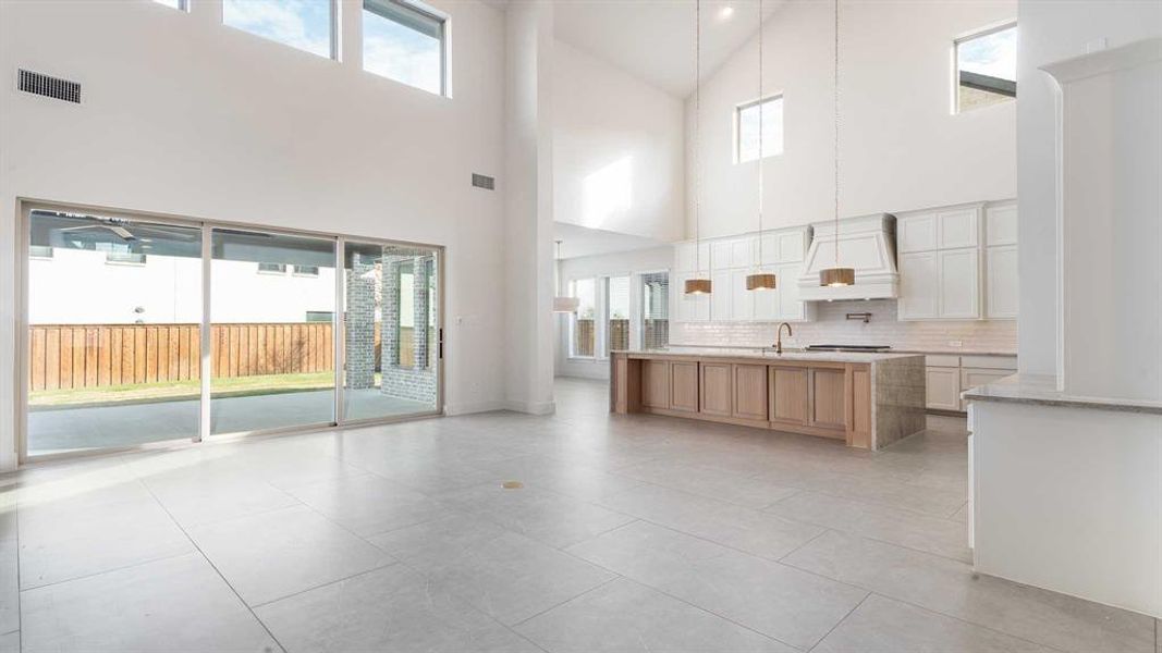 Kitchen featuring sink, light tile patterned floors, a towering ceiling, white cabinets, and custom exhaust hood