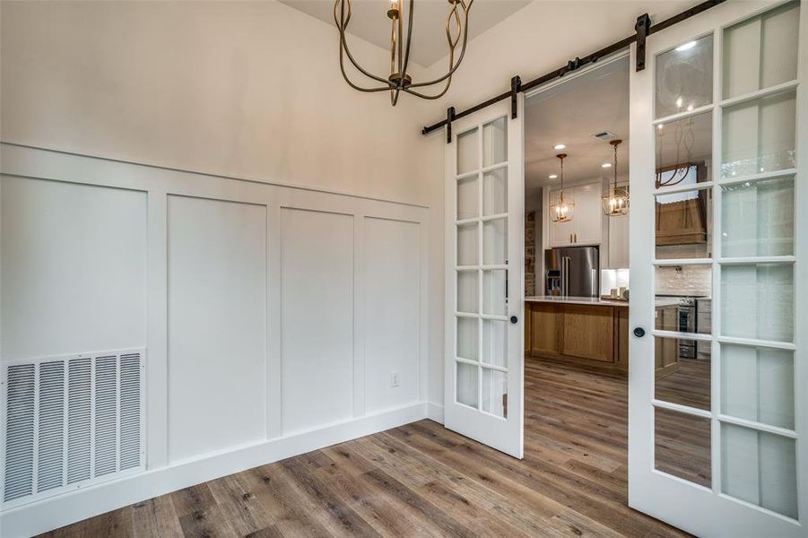 Unfurnished dining area with a notable chandelier, a barn door, wood-type flooring, and french doors