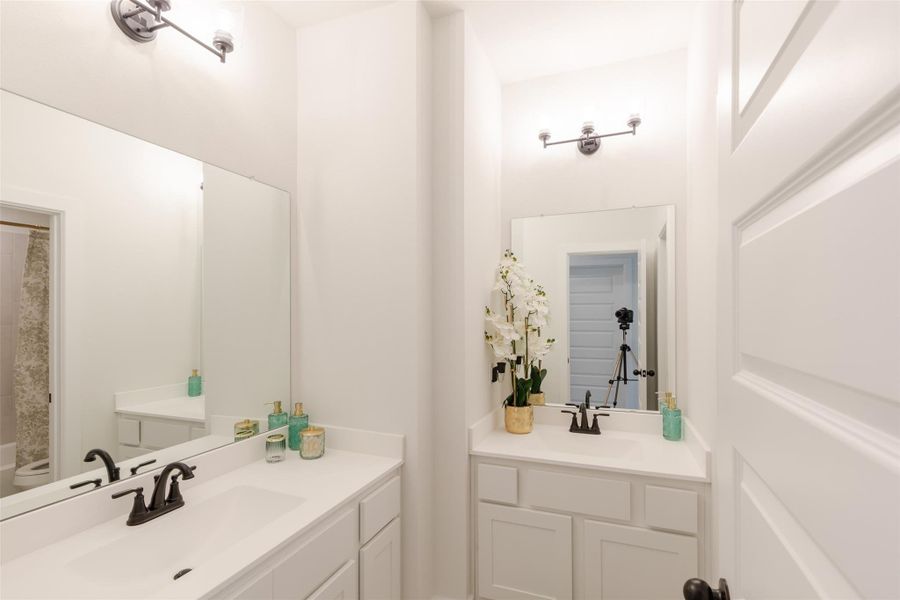 Modern bathroom with a clean design featuring white cabinetry, dual vanities, elegant lighting, and stylish black fixtures