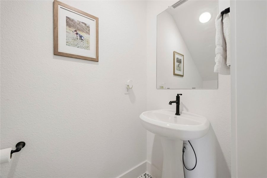 Just off the entry, a charming powder room welcomes guests with a classic pedestal sink, warm recessed lighting, and decorative tile flooring that adds character and style. Just off the entry, a charming powder room welcomes guests with a classic pedestal sink, warm recessed lighting, and decorative tile flooring that adds character and style.