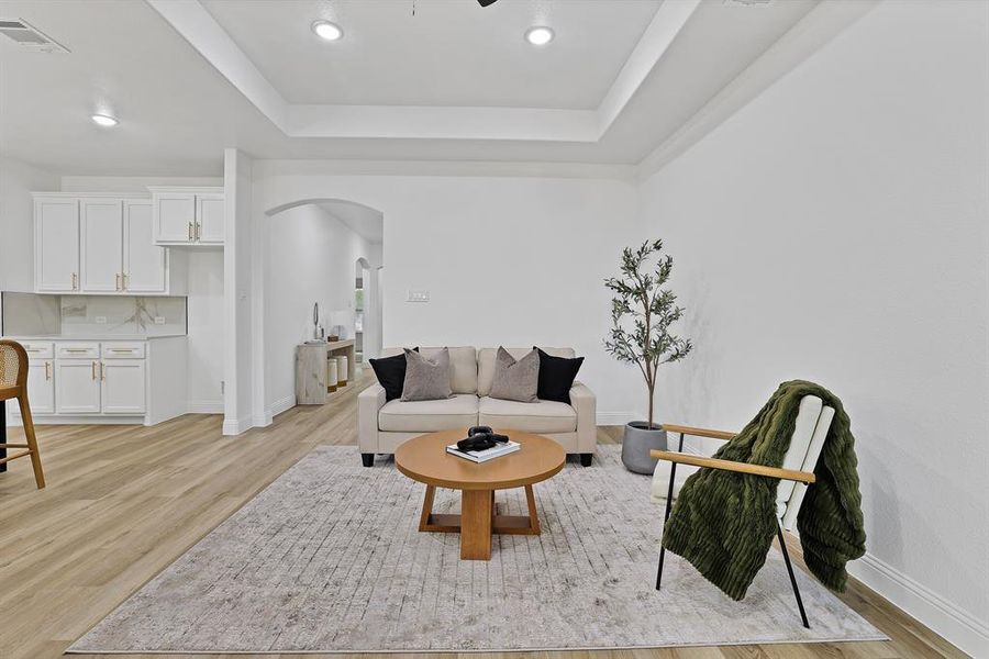 Living room with a tray ceiling and light wood-type flooring