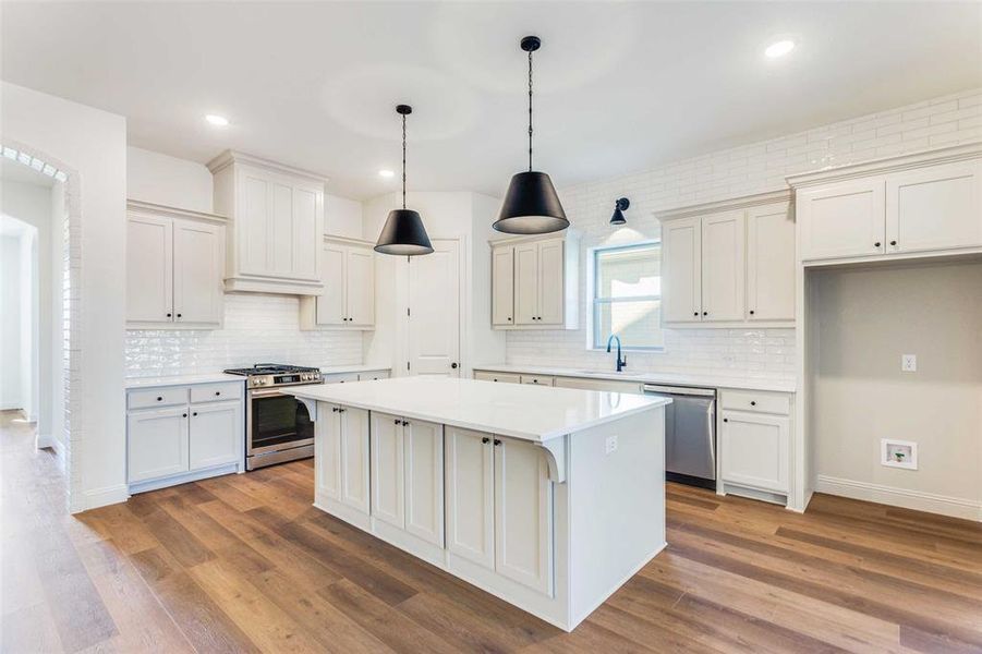 Kitchen featuring sink, a center island, tasteful backsplash, wood-type flooring, and appliances with stainless steel finishes